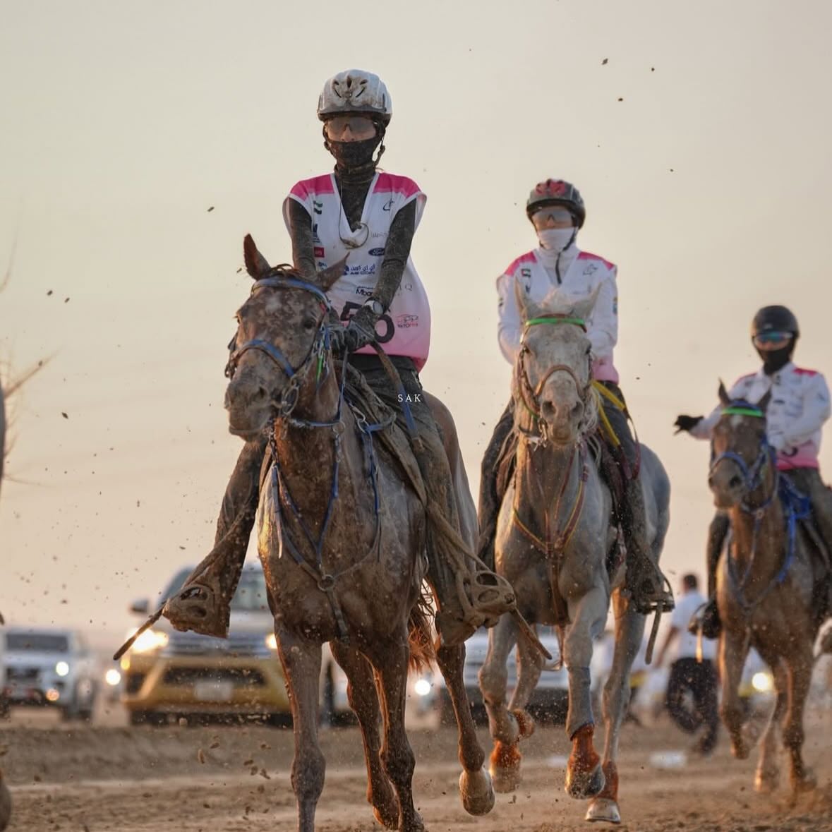 Two riders cantering side by side through the dust
